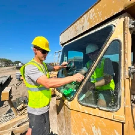 Two construction workers in yellow vests and hard hats operating machinery outdoors.