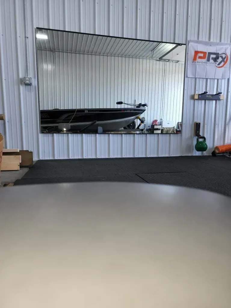 Boat reflected in a large mirror on a white wall. A dark floor is in the foreground.
