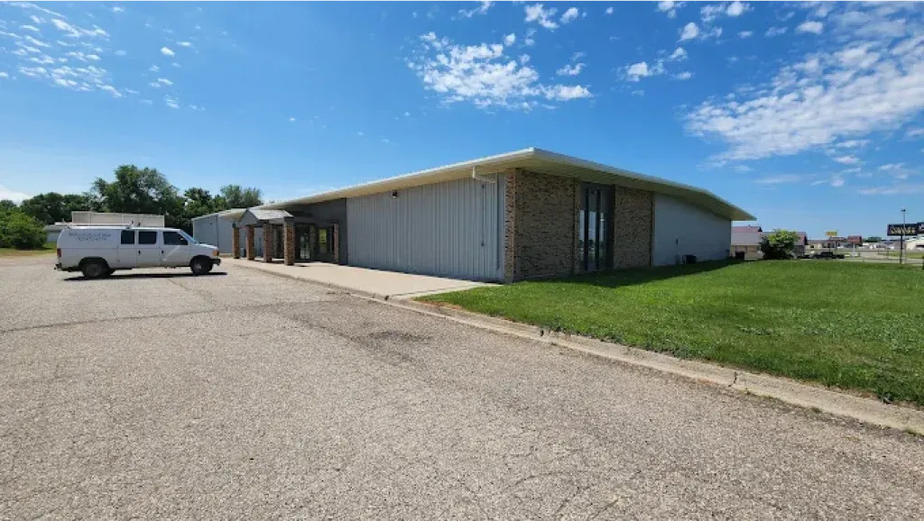 A light-colored commercial building with a white van parked in front on a sunny day.