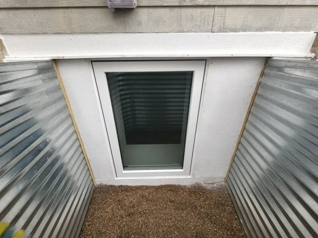 Window well with corrugated metal walls, white trim, and gravel.