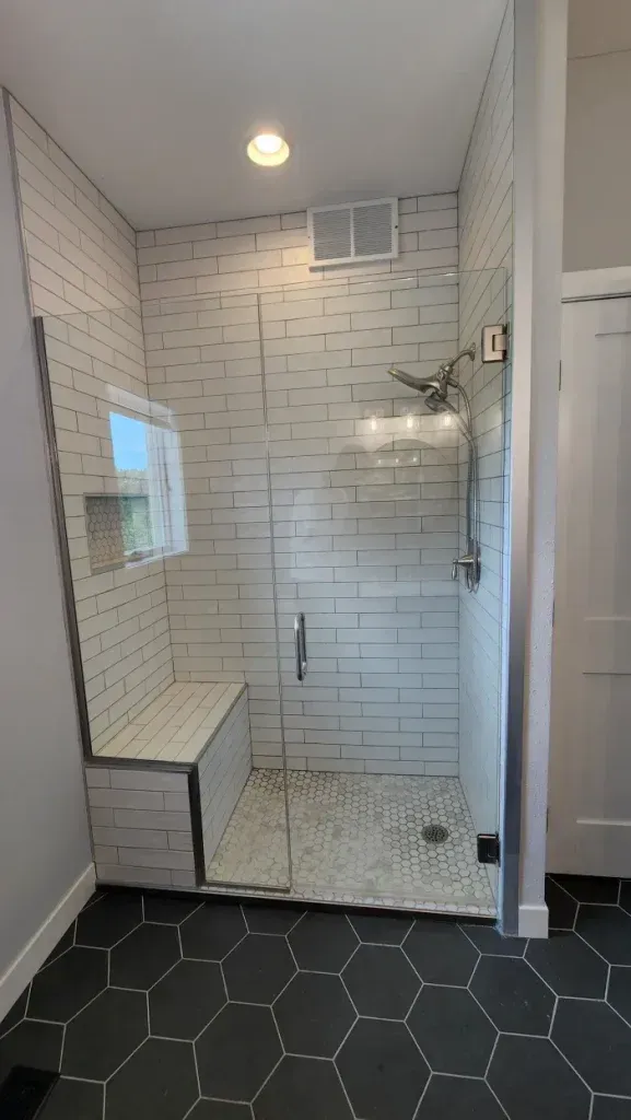 Modern bathroom with glass shower, white subway tile, stone floor, and a bench.