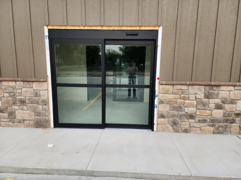 Automatic sliding glass doors at a building entrance with a person reflected in the glass.