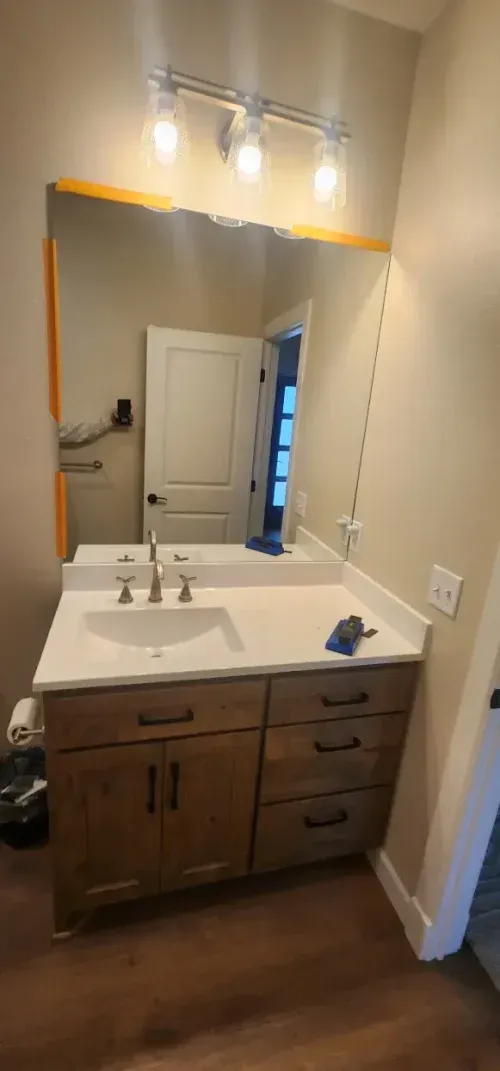 Bathroom vanity with a mirror, sink, and wood cabinetry. A door is reflected in the mirror.