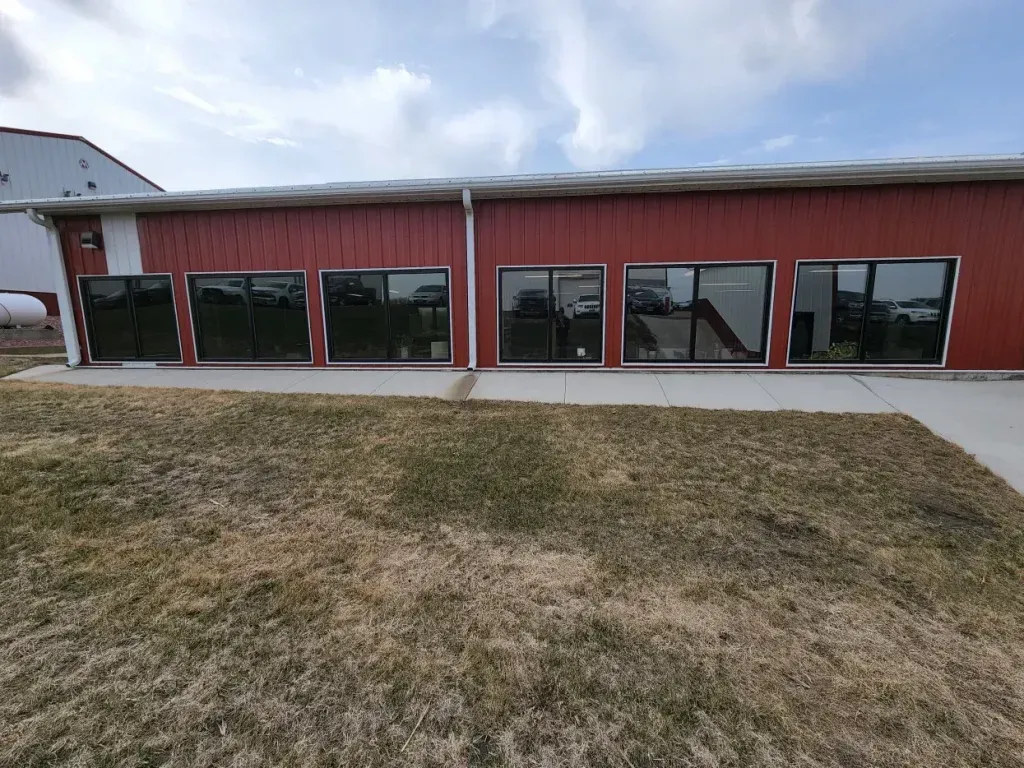 Red building with several windows and a gray concrete walkway; grass in the foreground, blue sky.