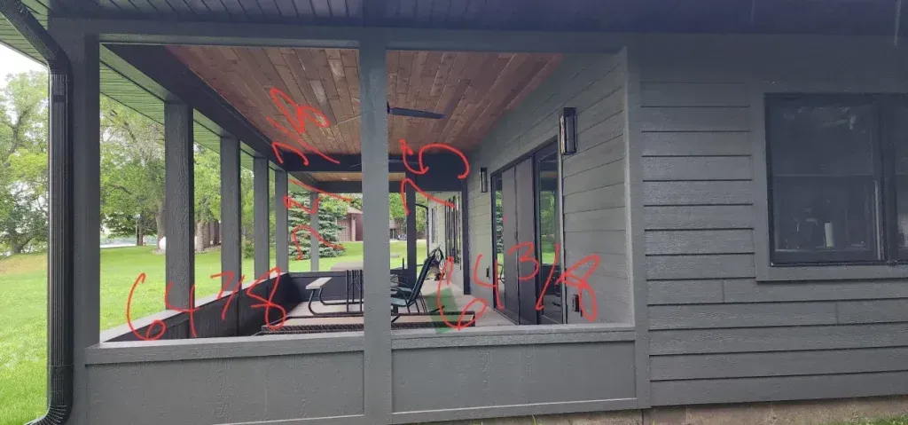 Exterior view of a porch with a wooden ceiling, gray pillars, and seating area.