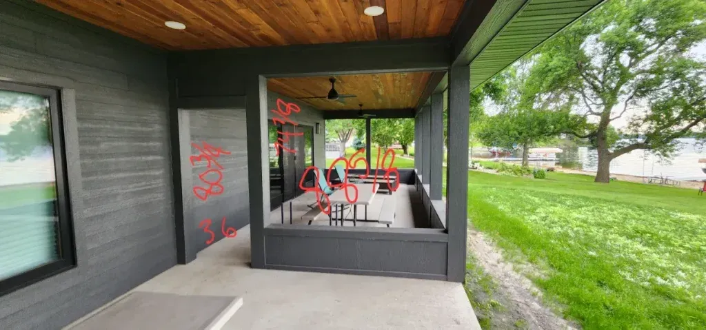 Exterior view of a modern house with a patio, overlooking a green lawn and trees.