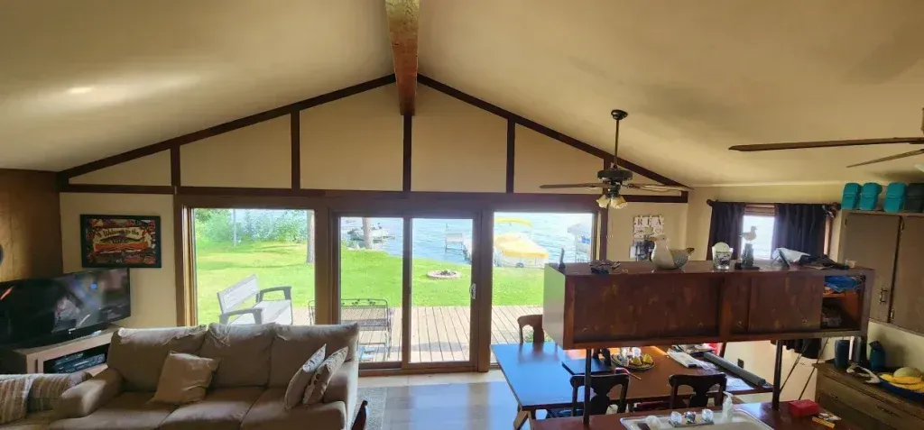 Living room with vaulted ceiling, large windows overlooking a green lawn. Sofa and dining table are visible.