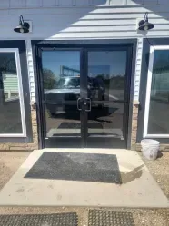 Double glass doors with black frames, exterior view, entrance with a doormat.