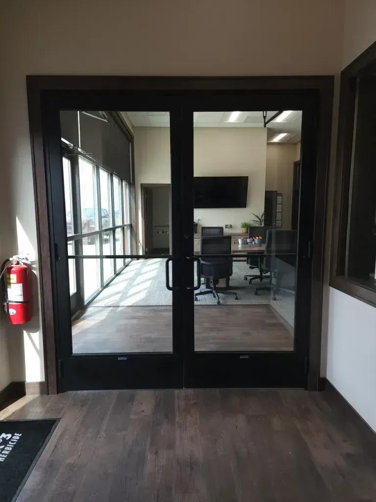 Double glass doors leading into an office with dark wood trim, a fire extinguisher on the left.