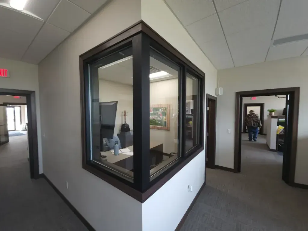 Interior office hallway with a corner window looking into an office space. Doors on either side.
