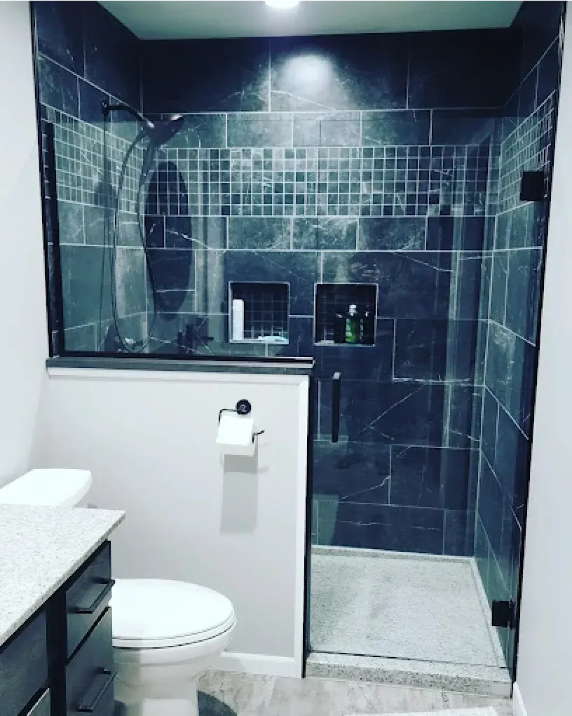 Modern bathroom with dark blue tiled shower, glass doors, toilet, and vanity.