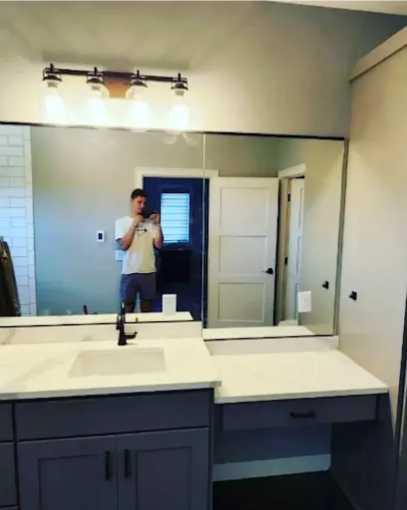 Man taking selfie in a newly renovated bathroom with a large mirror, gray cabinets, and white countertop.
