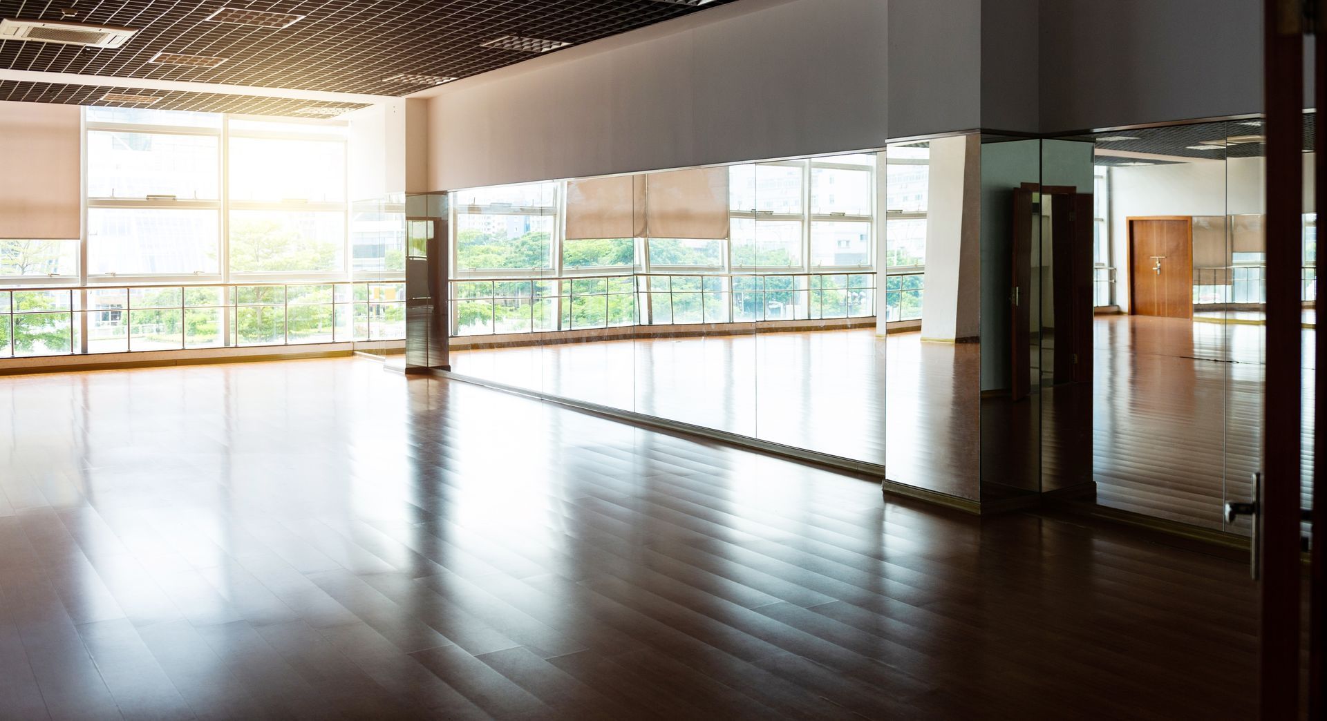 Empty dance studio with hardwood floor, large windows, and a mirrored wall.