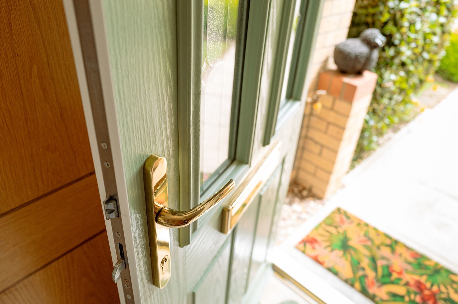 Light green front door with gold handle open to a porch with a welcome mat.