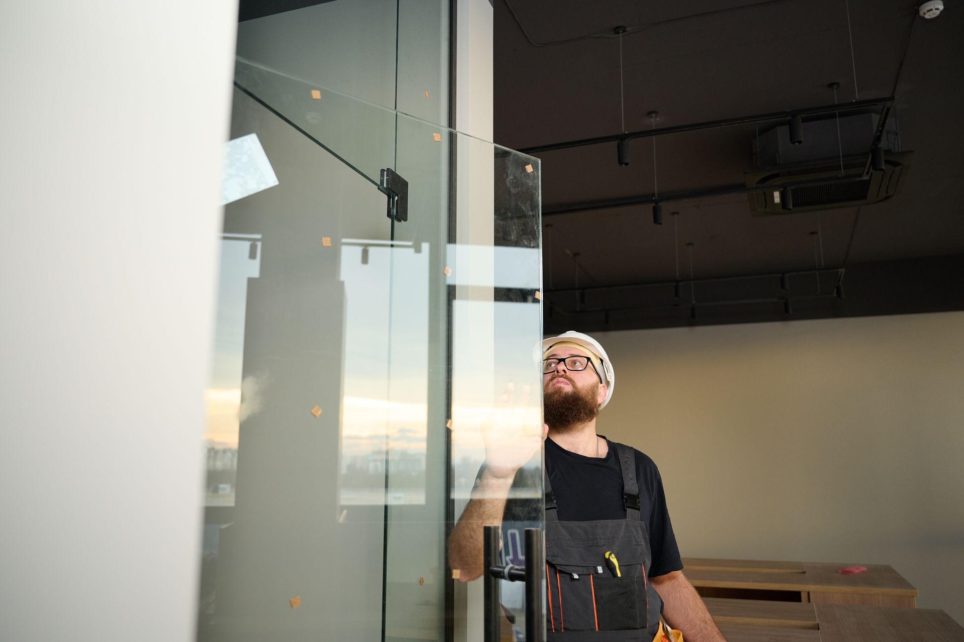 Man with beard and overalls installing a glass door in an office.