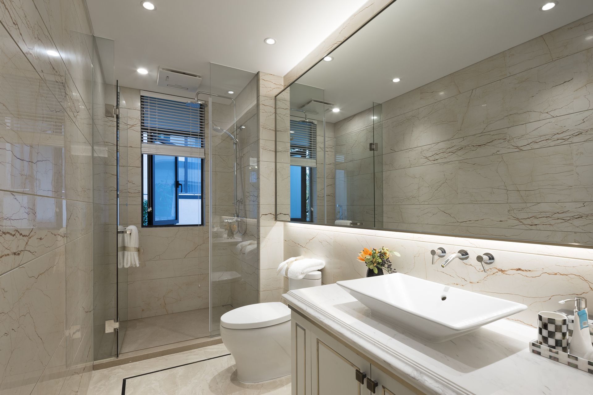 Luxurious bathroom with marble walls, glass shower, white toilet, and large mirror.