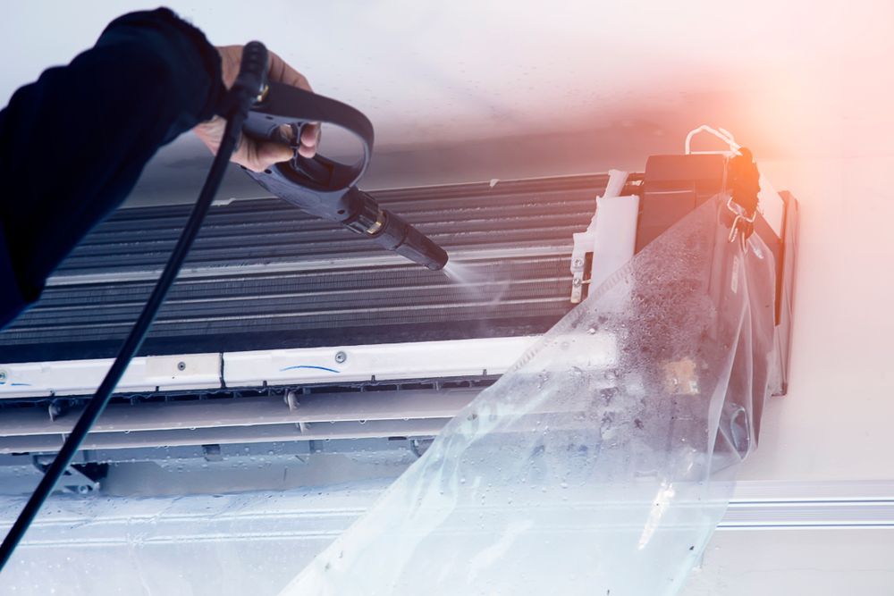 A Person Wearing Blue Gloves is Cleaning an Air Conditioner With a Brush — Breathe Easy Solutions In Jamboree Heights, QLD