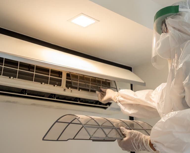 A Person Wearing Blue Gloves is Cleaning an Air Conditioner With a Brush — Breathe Easy Solutions In Jamboree Heights, QLD