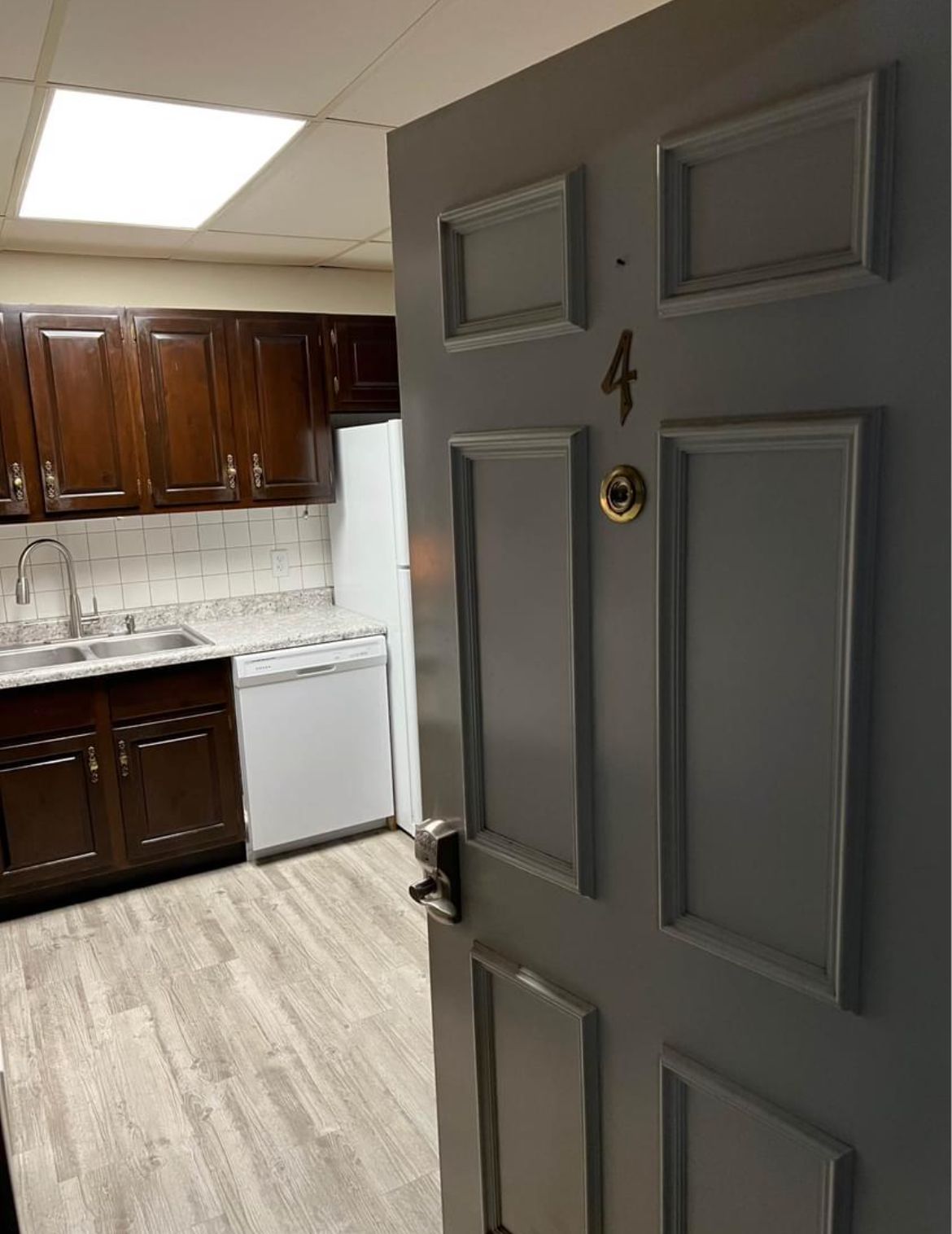 A gray door is open to a kitchen with wooden cabinets and a refrigerator.