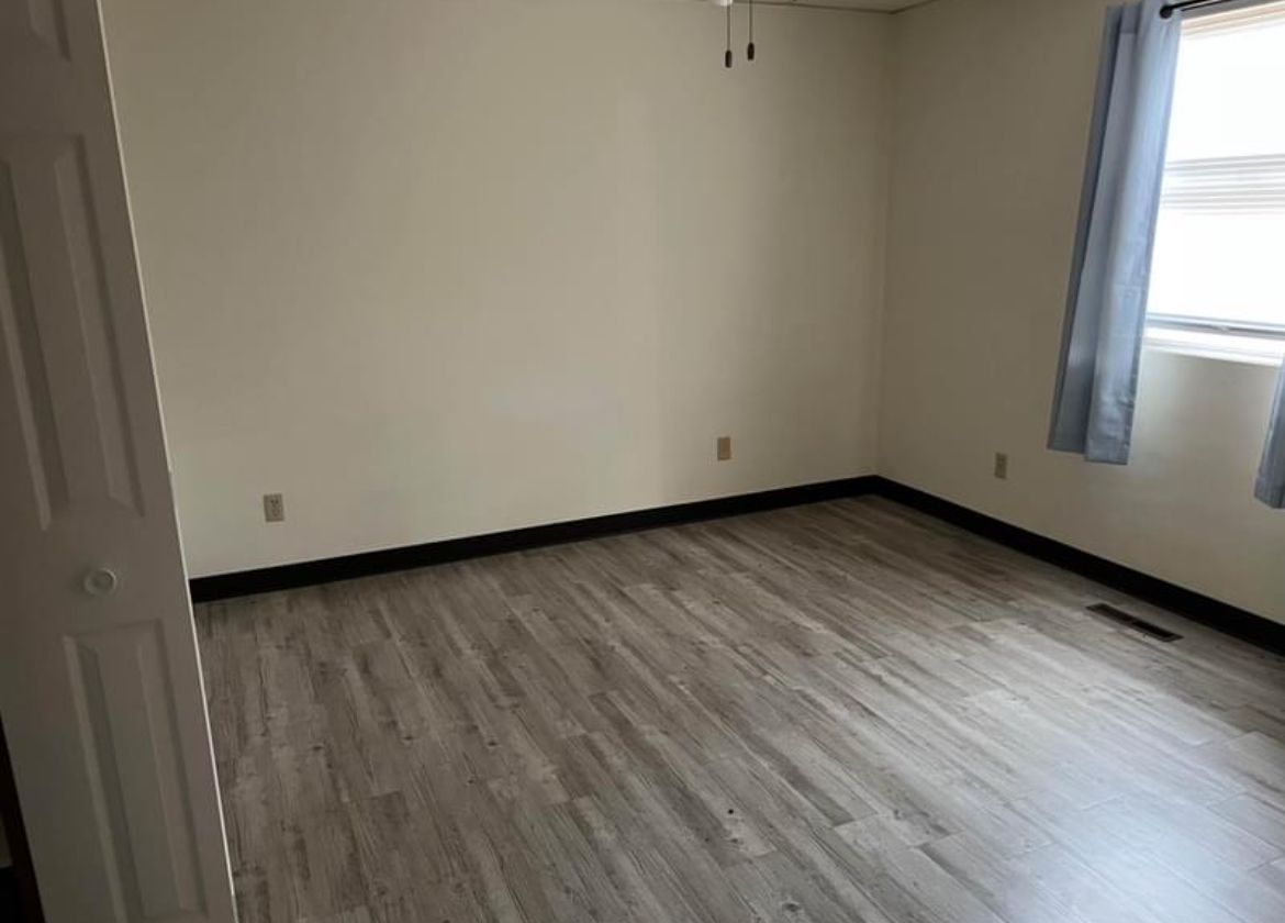 An empty room with hardwood floors and white walls.