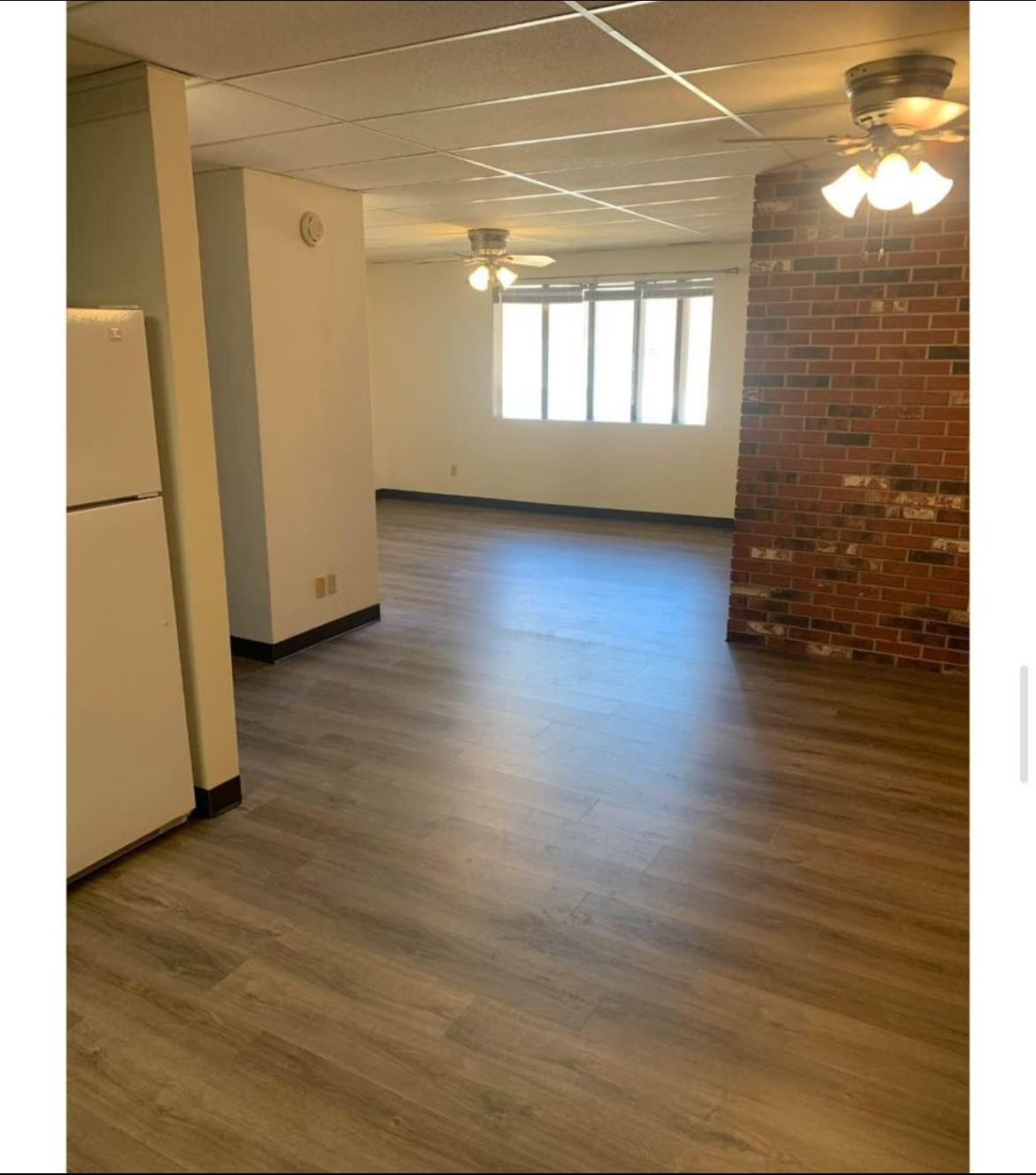 A large empty room with hardwood floors and a brick wall.