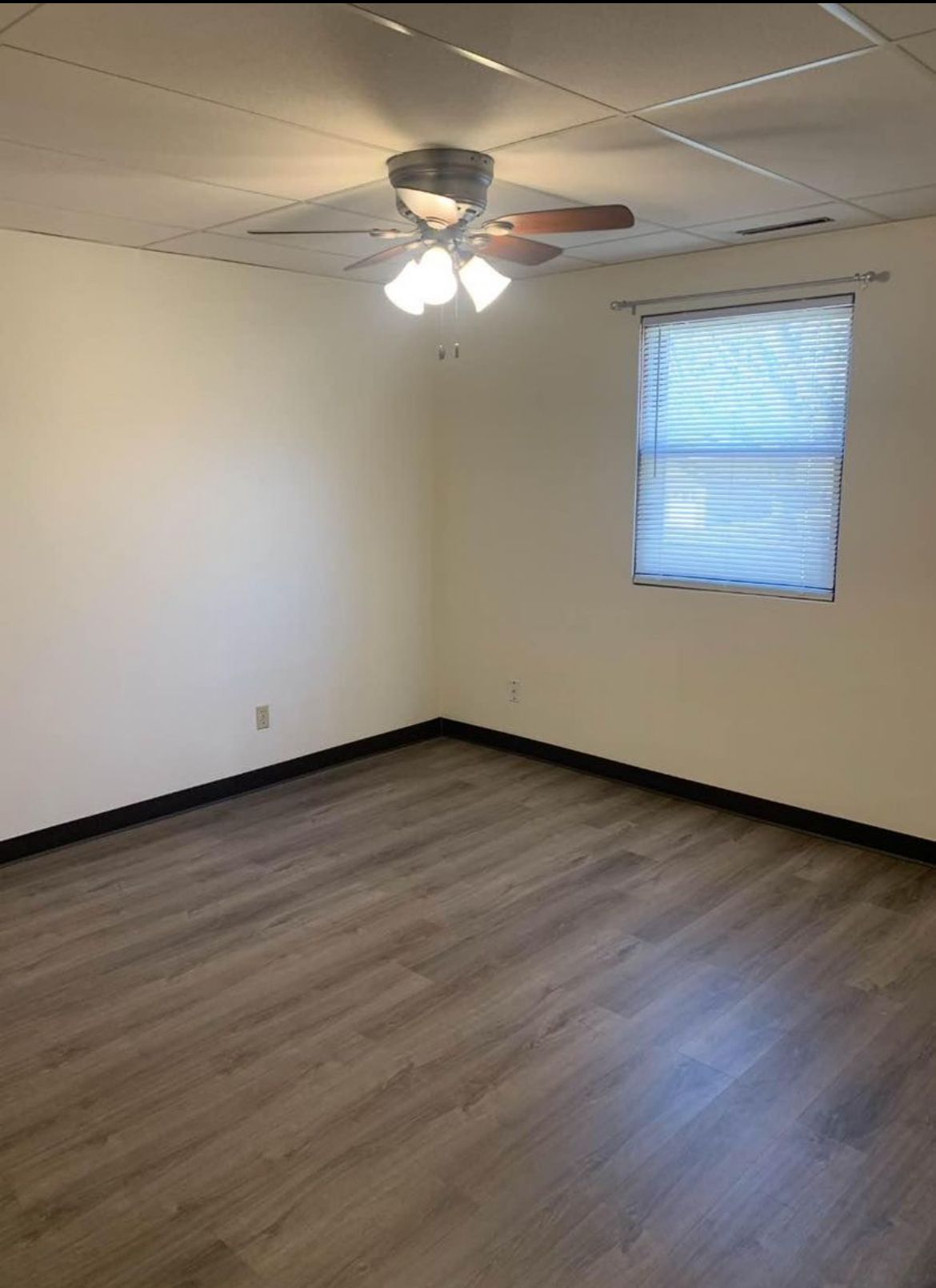 An empty room with a ceiling fan and a window.