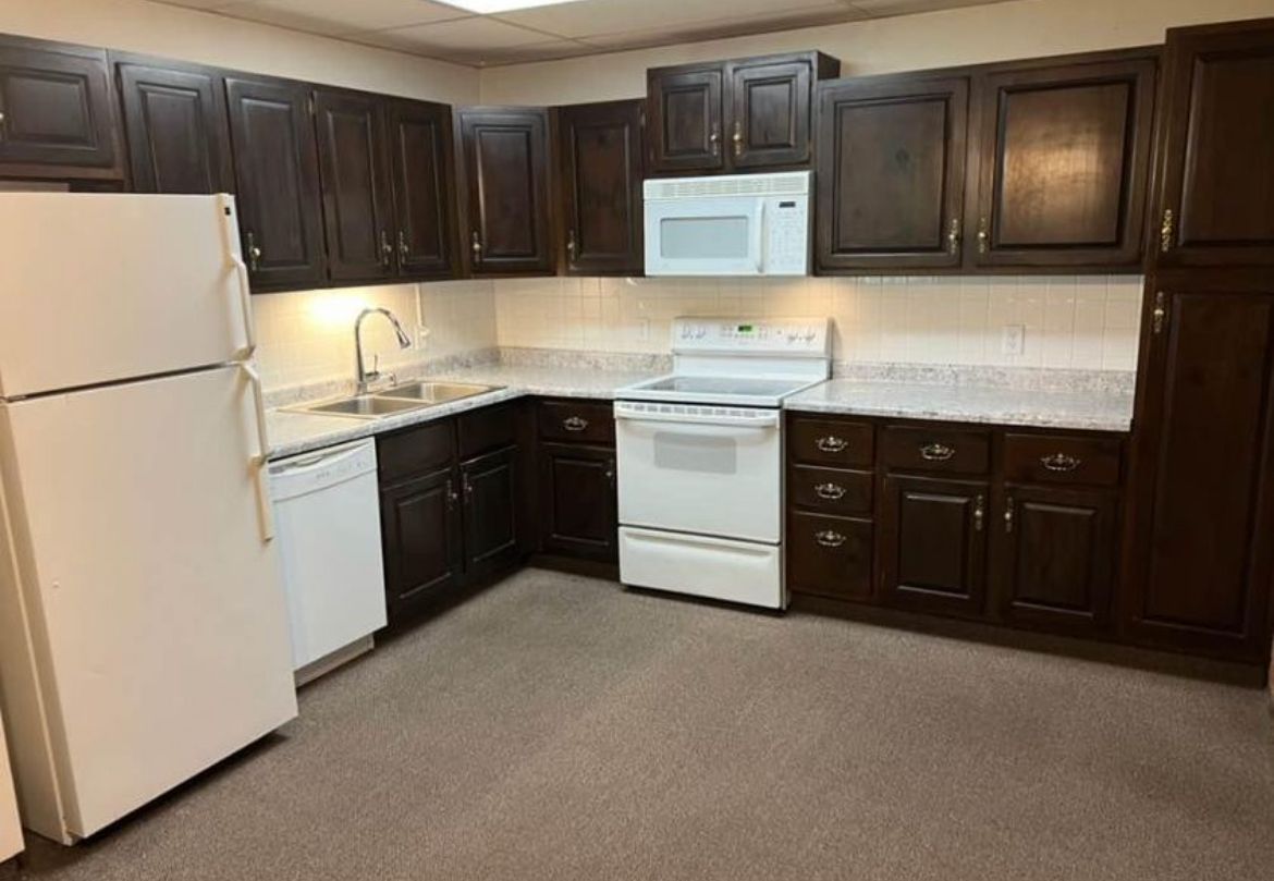 A kitchen with brown cabinets , white appliances , and a refrigerator.
