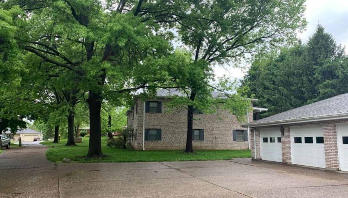 A brick house with a garage and trees in front of it.