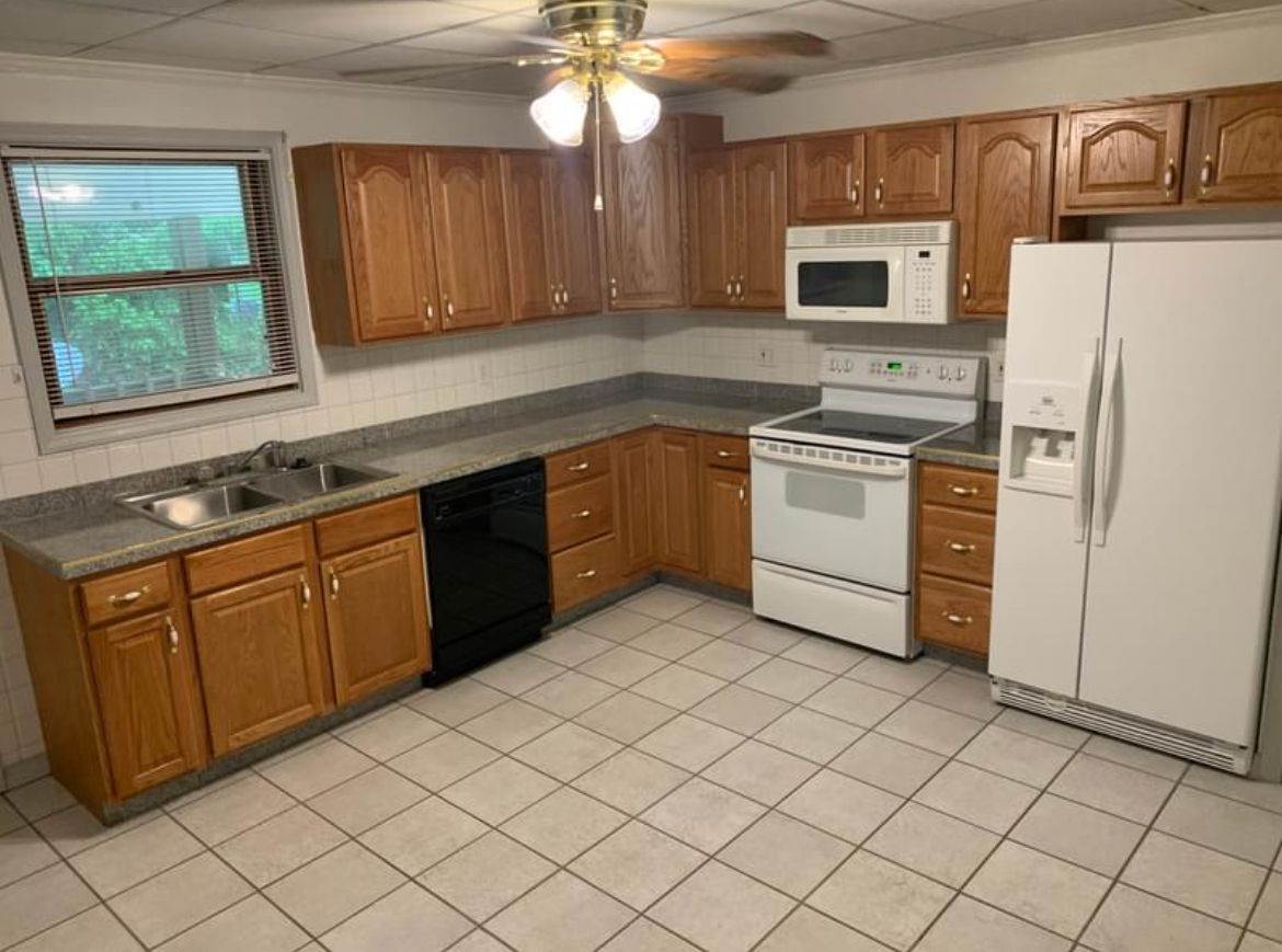 A kitchen with wooden cabinets , a refrigerator , stove , microwave and sink.