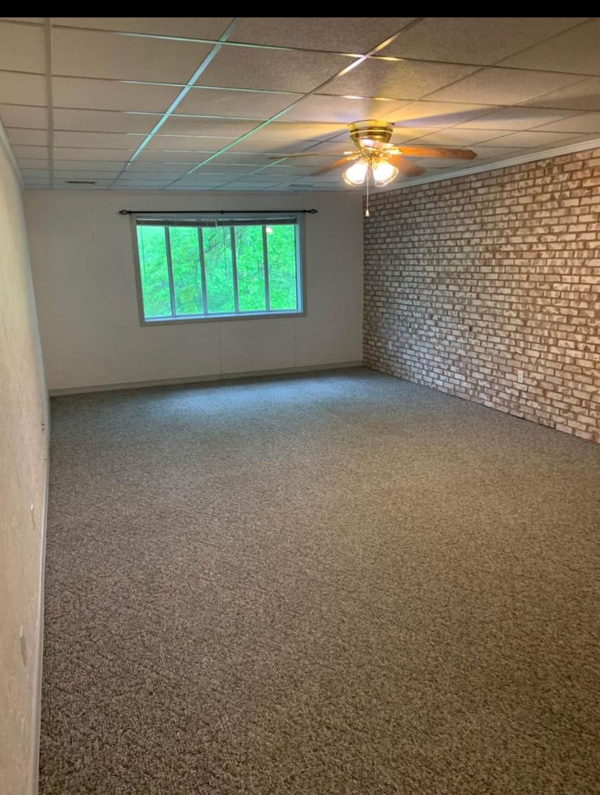 An empty living room with a ceiling fan and a brick wall.