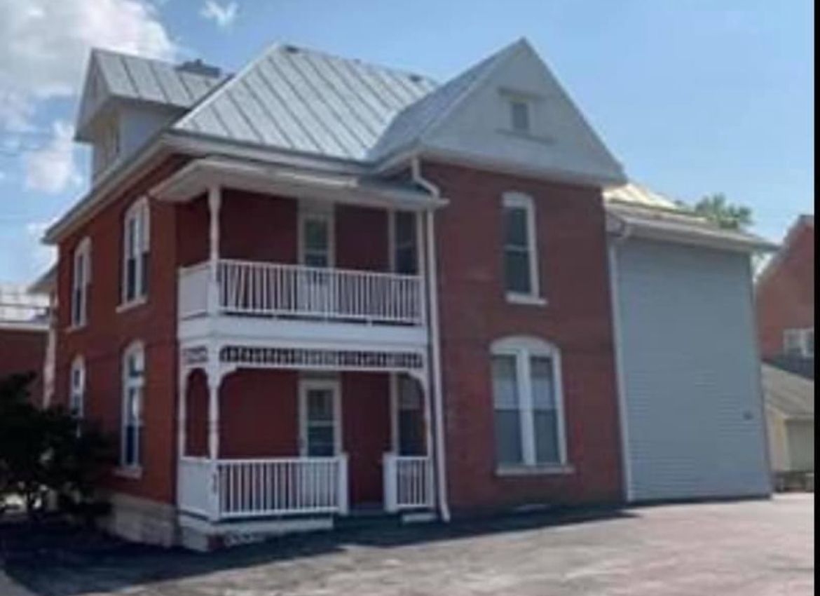 A red brick house with a white porch and a metal roof