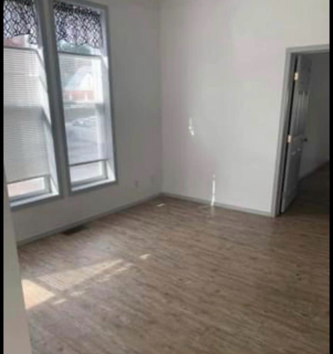 An empty living room with hardwood floors and two windows.