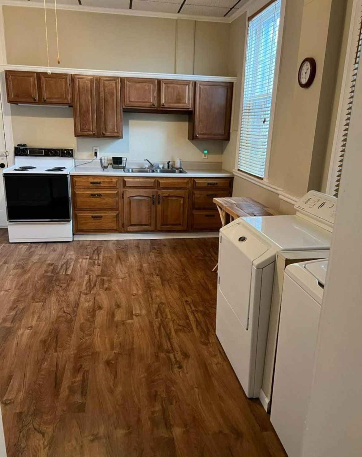 A kitchen with wooden cabinets , a stove , a washer and dryer , and a window.