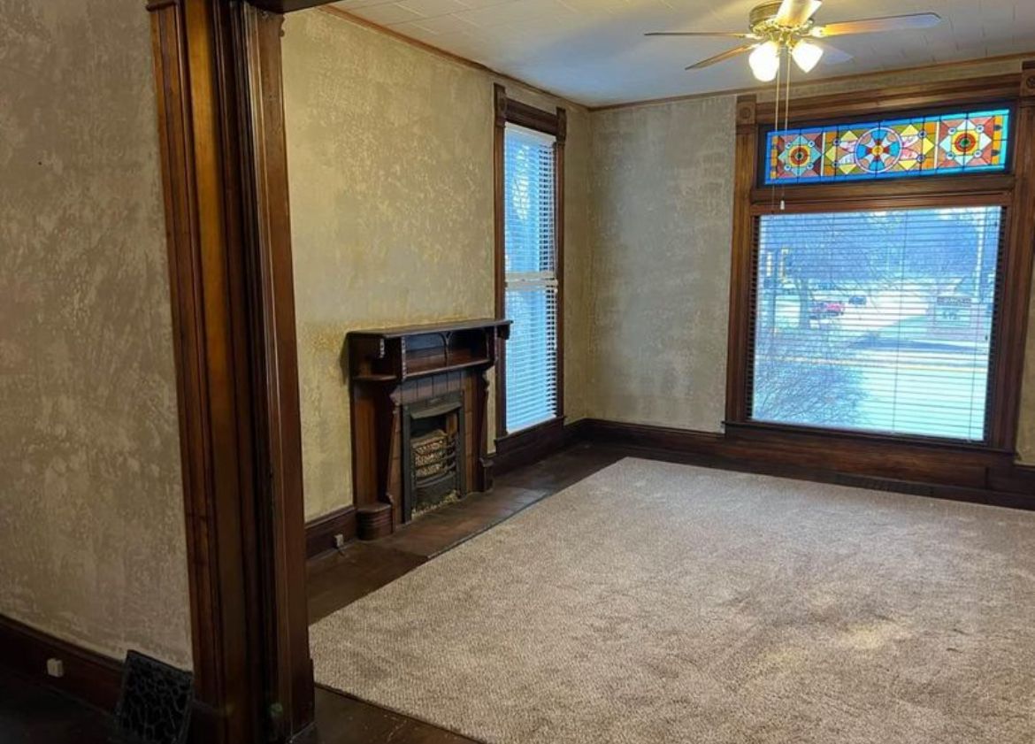 An empty living room with a fireplace and a ceiling fan.