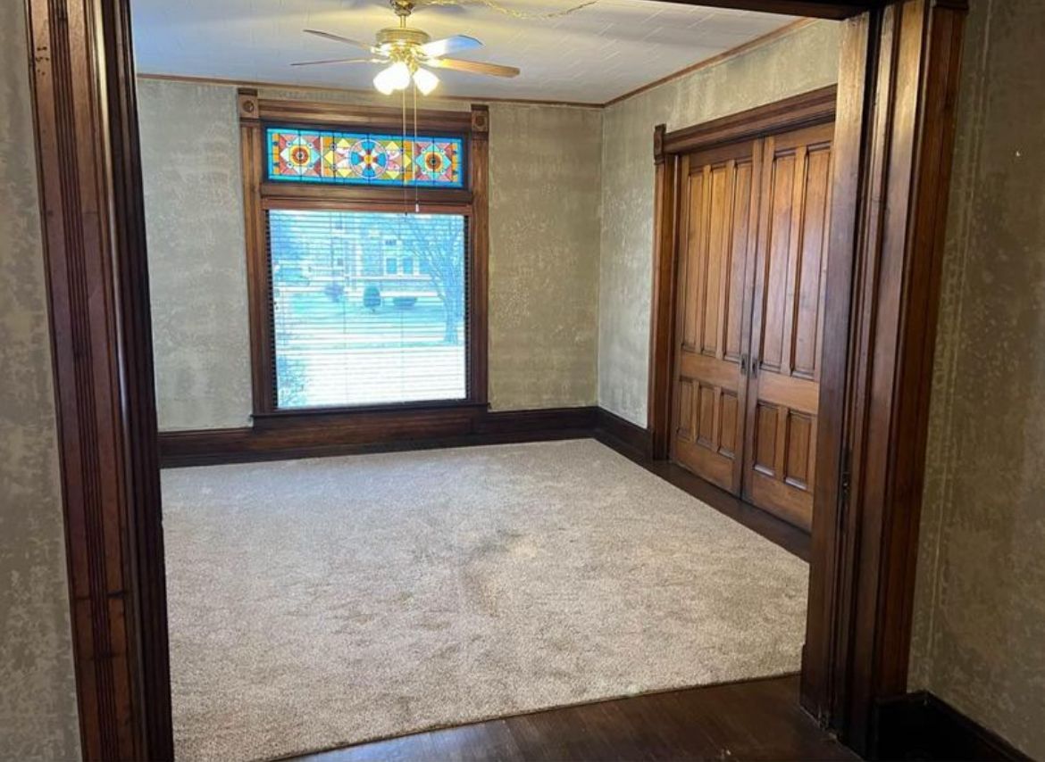 An empty room with a ceiling fan and a window.
