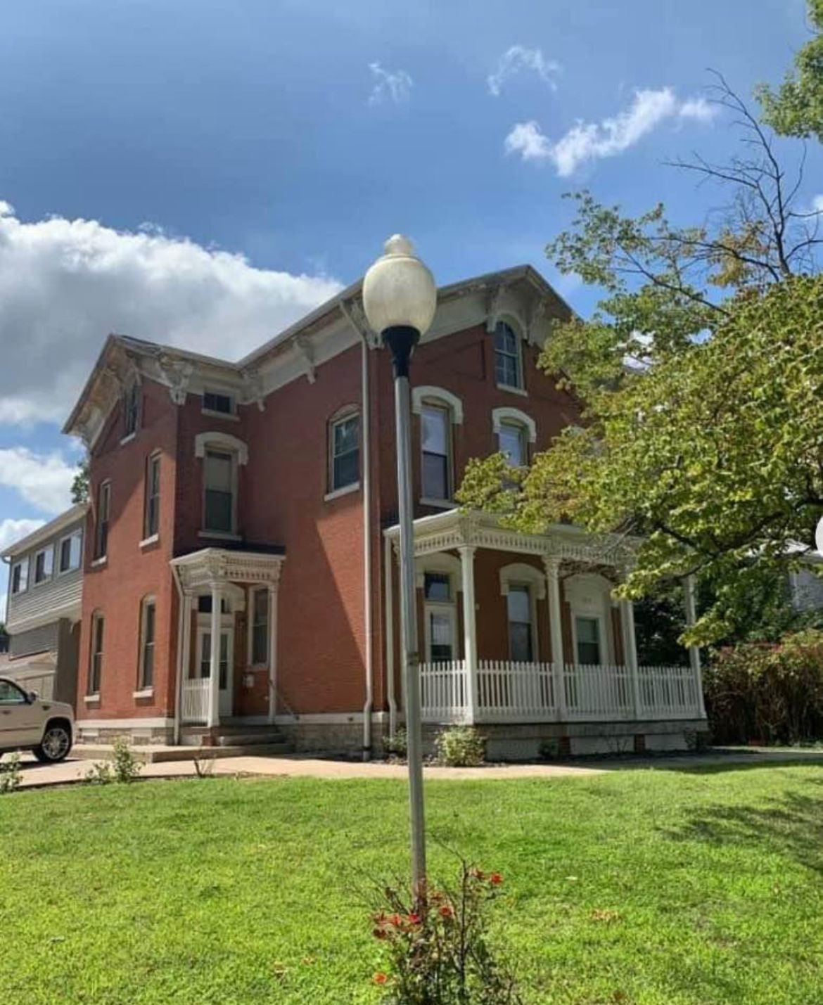 A large red brick house with a white porch and a lamp post in front of it.