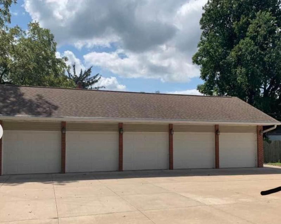 A large garage with four white garage doors and a brown roof.