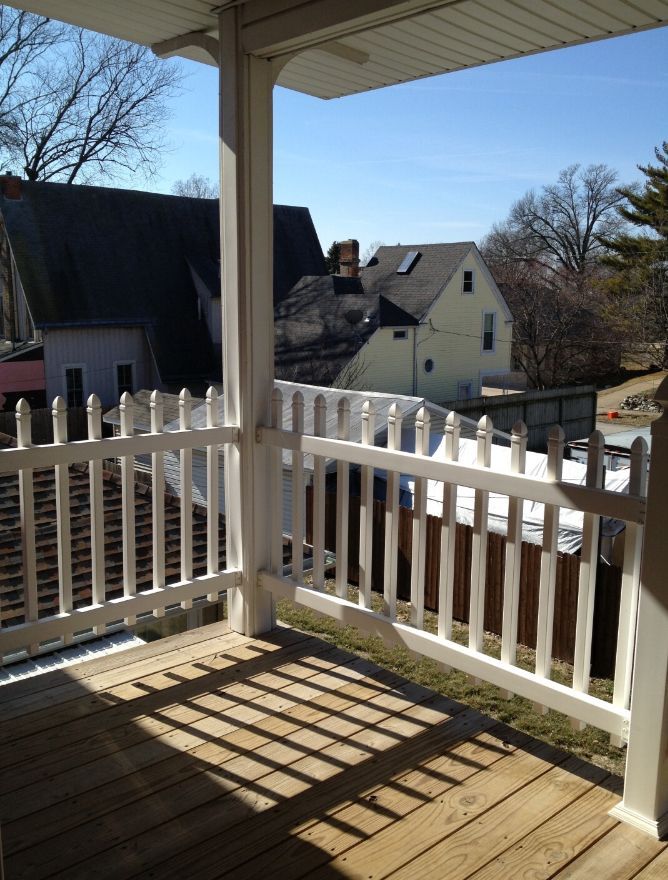 A porch with a white picket fence and a view of a house