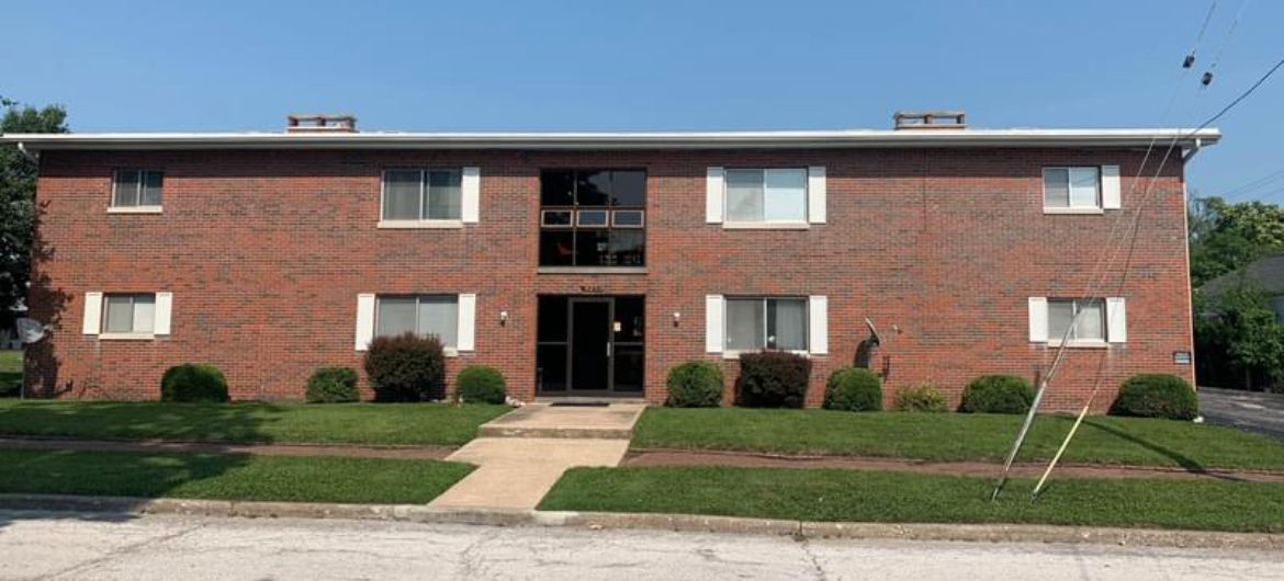 A large brick apartment building with a lush green lawn in front of it.