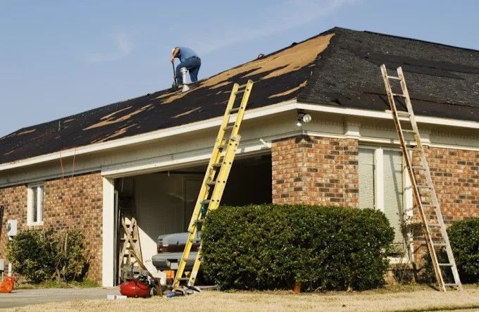 Roofer on a house removing shingles, working on roof repair with two ladders.