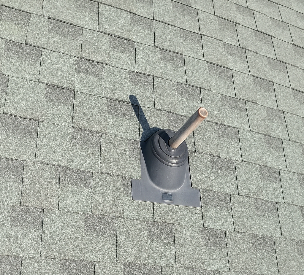 A pipe is sitting on top of a roof with shingles.