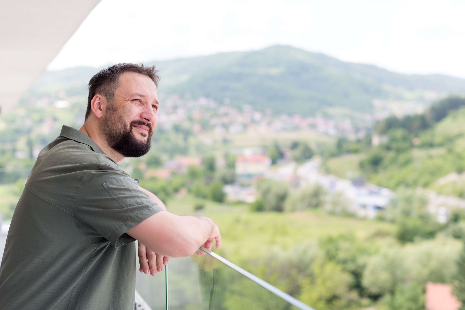 A successful-looking, happy man smiling and looking out from a modern balcony with a city and mountains in the background, symbolizing hope and positive outcomes after effective therapy.