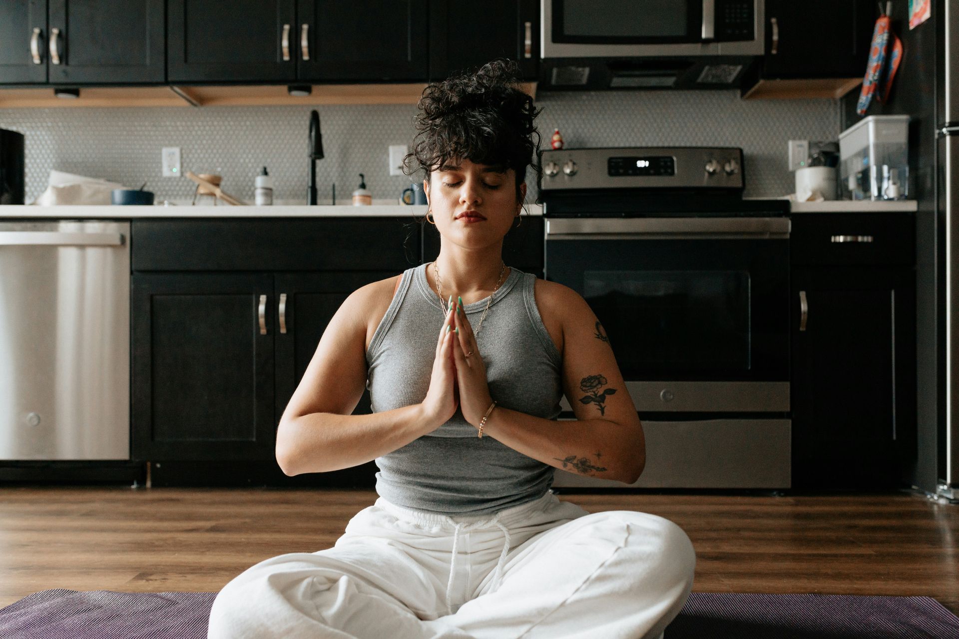 Person sitting in meditation pose on a yoga mat in a kitchen, practicing emotion regulation skills.