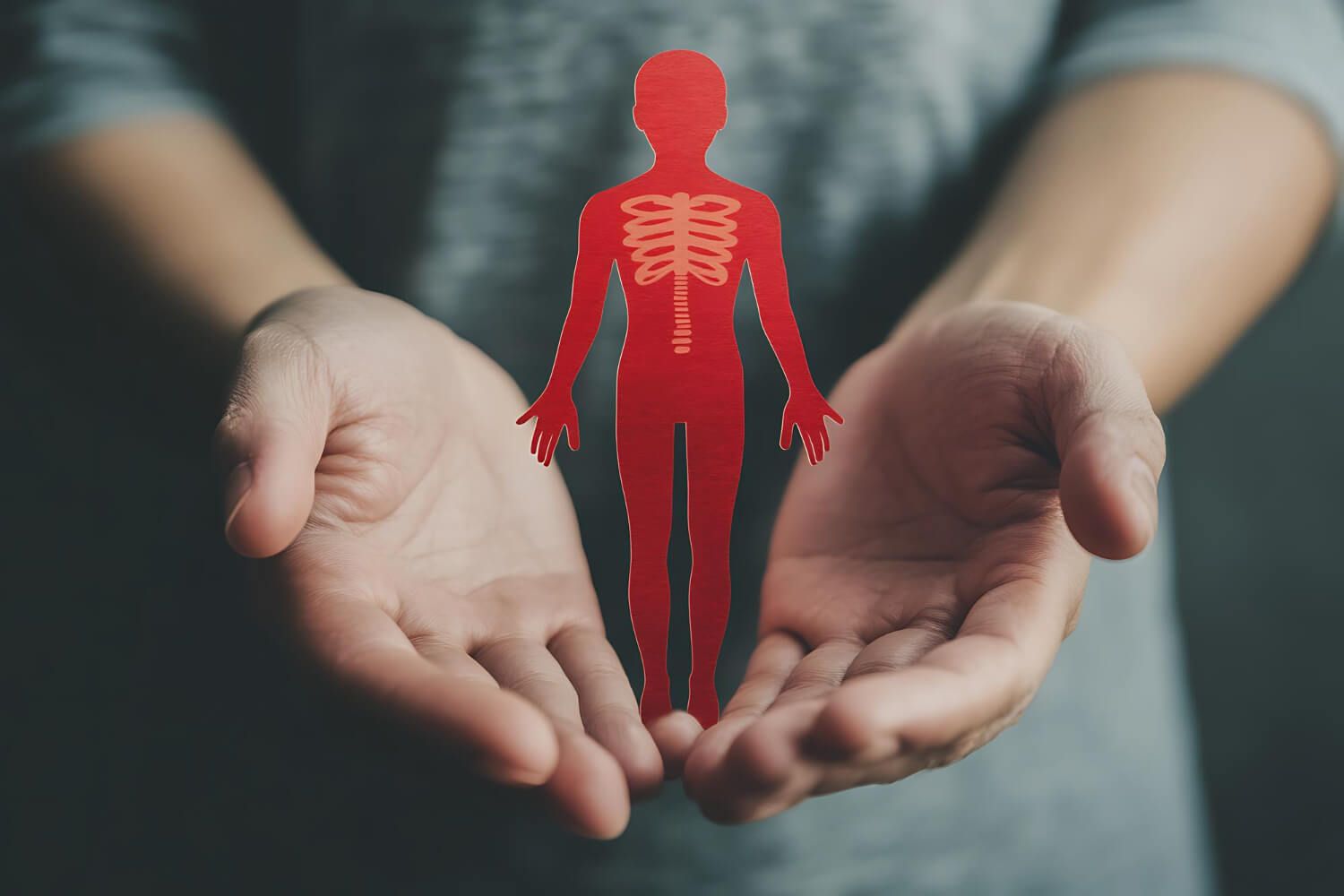 Two hands gently cupping and protecting a red human silhouette figure representing nervous system care and self-compassion