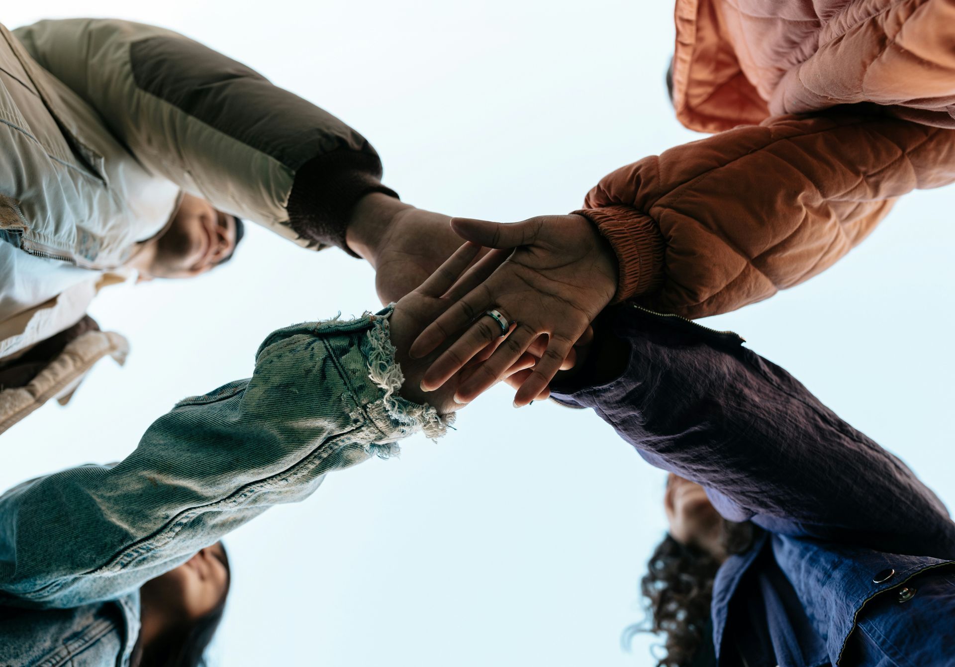 Multiple hands joining together in a circle viewed from below, representing the integration of different parts in Internal Family Systems therapy.