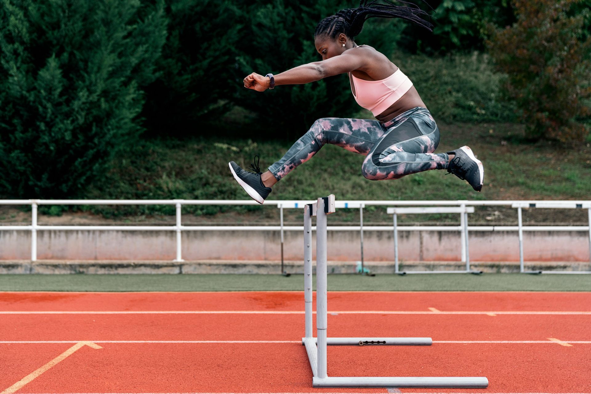 Person in athletic wear mid-jump clearing a hurdle on a running track, representing the physical aspects of overcoming emotional challenges and the mind-body connection in trauma recovery.