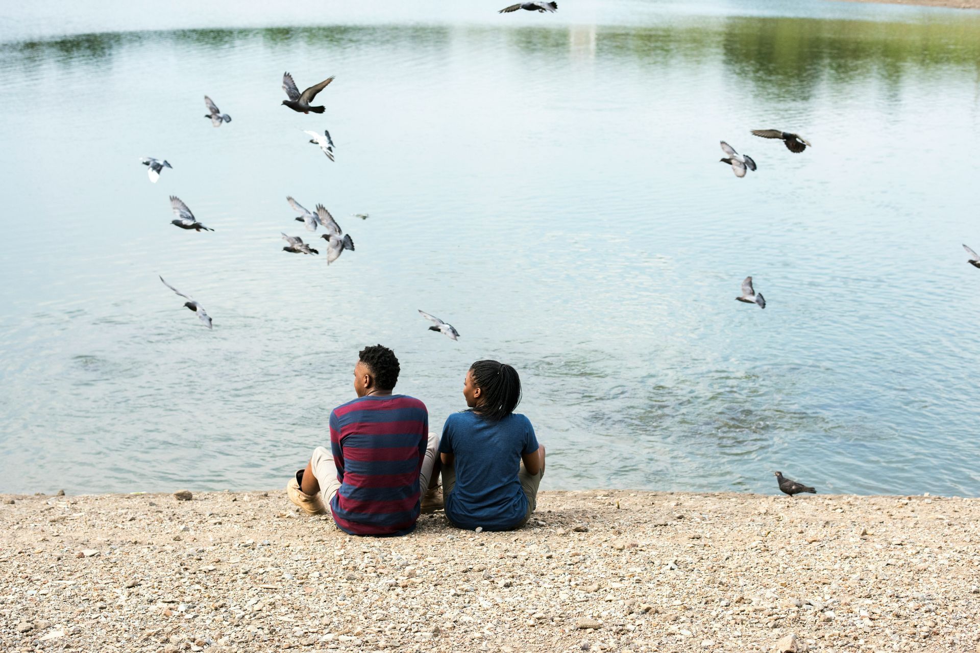 Two people sitting peacefully by a lake watching birds fly freely over the water, symbolizing the mental freedom that comes with breaking free from thinking traps.