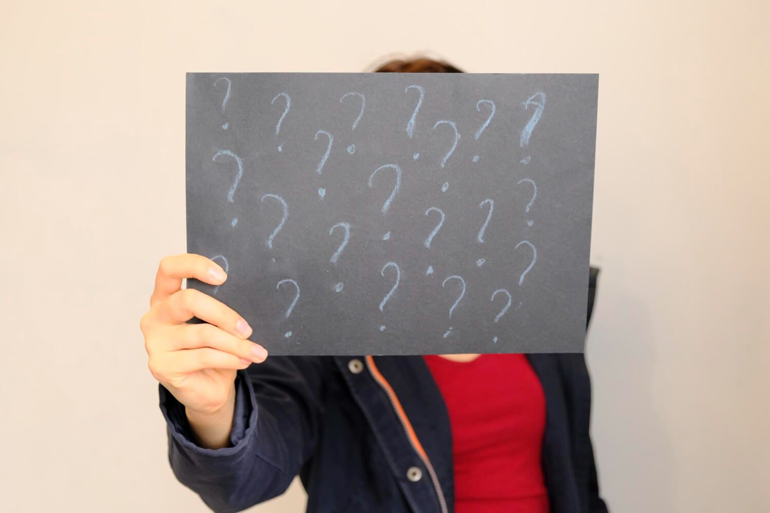 Person holding chalkboard covered with white question marks representing common questions about somatic therapy and trauma treatment