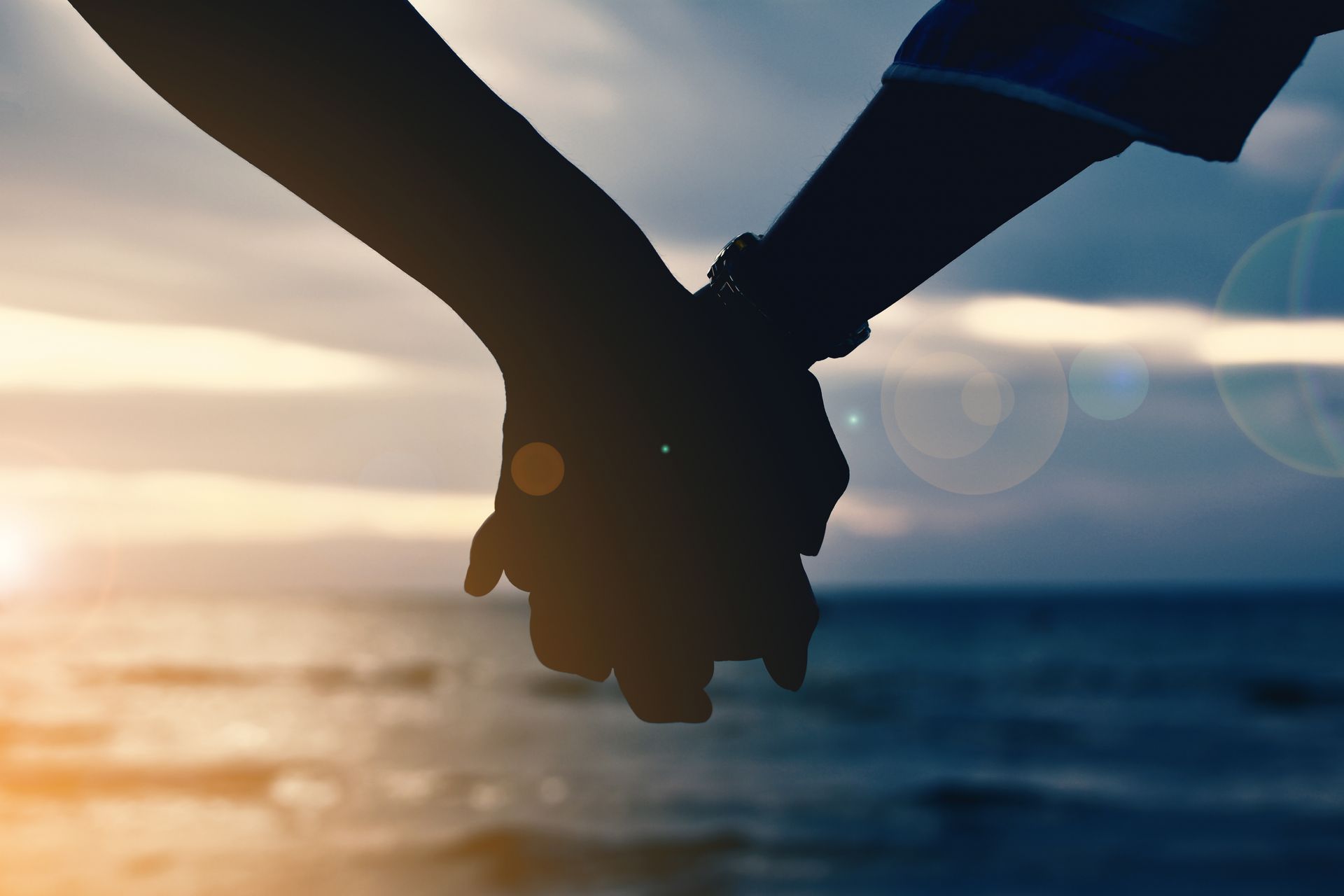 Silhouette of two people holding hands against sunset background, symbolizing healing connection