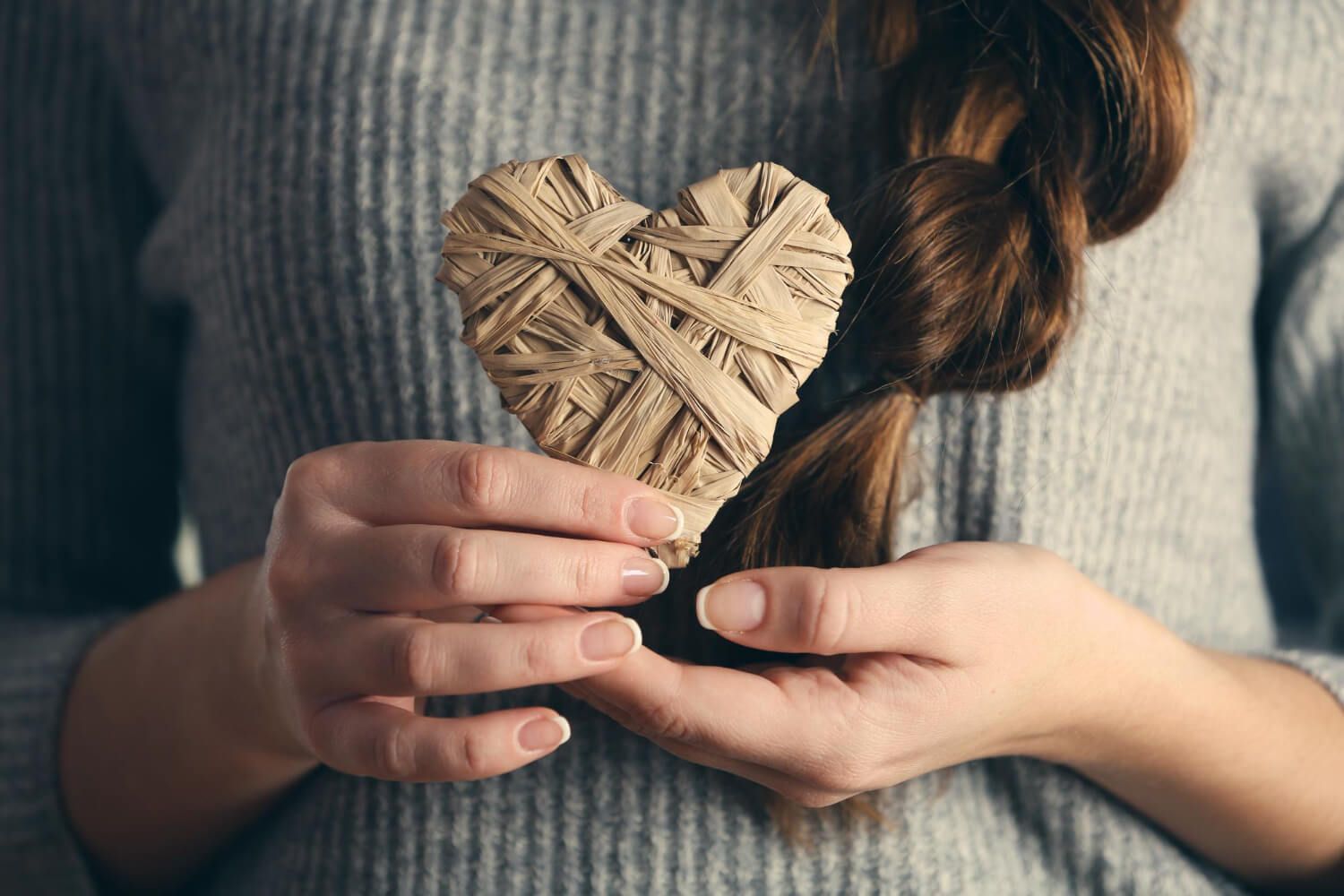 Hands gently holding handcrafted woven heart symbolizing self-compassion and healing through Internal Family Systems therapy
